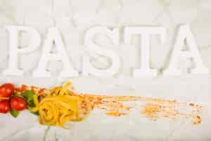 Free photo pasta word with cherry tomato and basil leaf