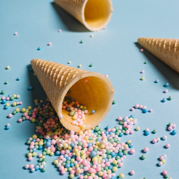 Free Photo pastel colored sprinkles spilling from waffle cone on blue background