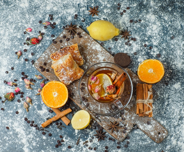 Free photo pastries with flour, tea, choco, biscuits, spices, lemon, orange, herbs top view on concrete and cutting board