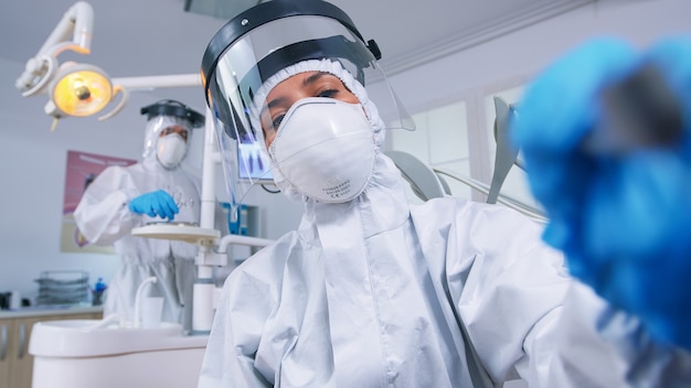 Patient pov while dentist in ppe suit against covid is working on tooth hygine in dental office with new normal. Stomatolog wearing safety gear against coronavirus during heatlhcare check of person.