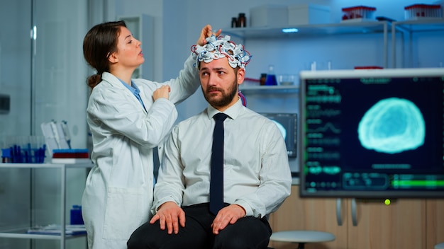 Free photo patient with brain scan discussing with researcher neurological doctor while adjusting brainwave scanning headset examining diagnosis of disease, explaning eeg results, health status, brain functions