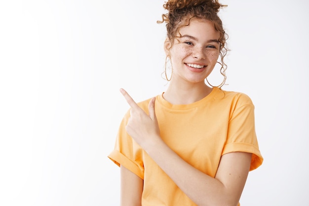 Free photo pay visit place that direction friendly charismatic smiling pleasant redhead girl show interesting place cool product promoting copy space pointing upper left corner standing white background