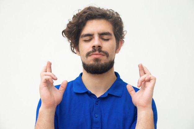 Peaceful guy with closed eyes keeping fingers crossed