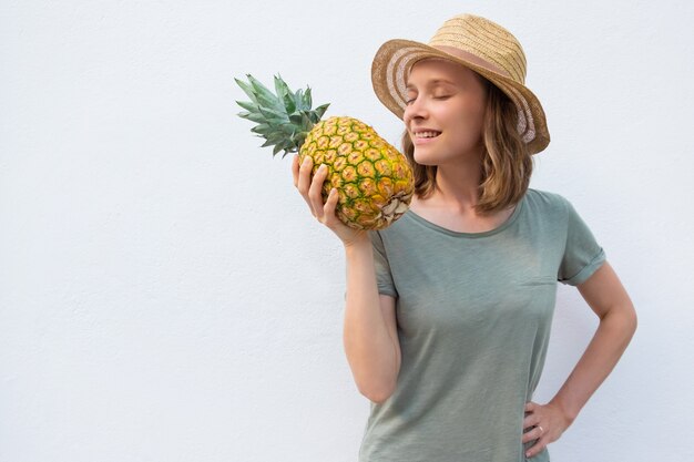 Peaceful inspired woman in summer hat smelling whole pineapple