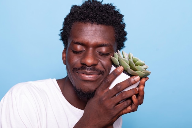 Peaceful man holding small pot with plant and smiling