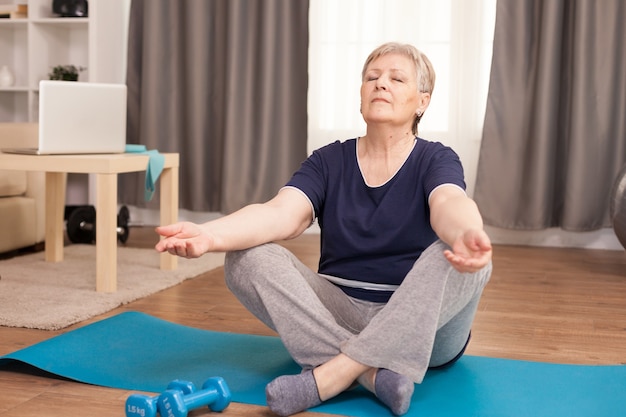 Peaceful senior woman with eyes closed doing yoga in living room