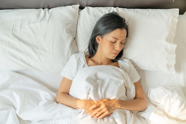 Peaceful serene young lady wear pajamas lying asleep on the bed. Top view