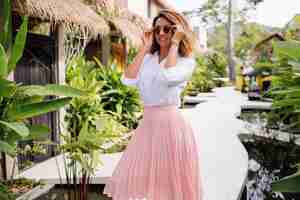 Free photo peaceful young happy woman with short curly hair in pink long skirt and white shirt alone outside her villa