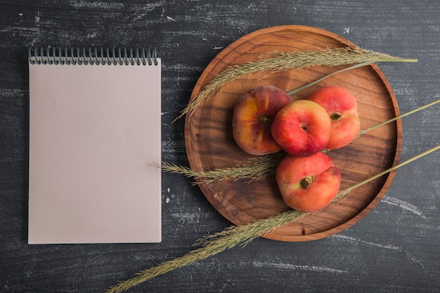 Peaches with herbs or spices on a wooden platter with a notebook aside