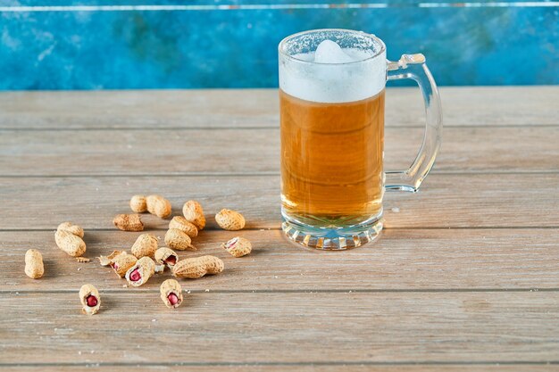 Peanuts and a glass of beer on wooden table.