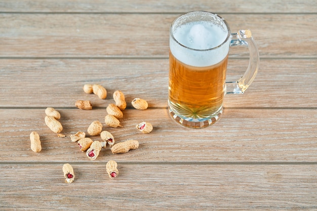 Peanuts and a glass of beer on wooden table.