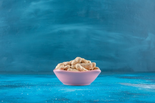 Peanuts in shell in a plate on the blue surface