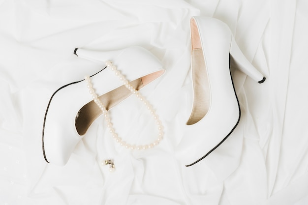 Free photo pearl necklace and earrings with pair of wedding high heels on scarf