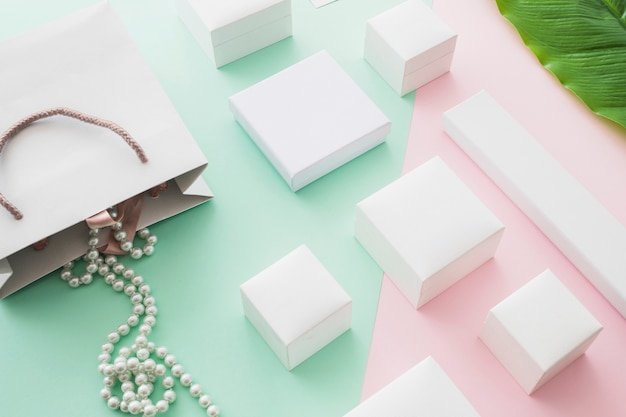 Free Photo pearls necklace falling from shopping bag with white boxes on pastel background