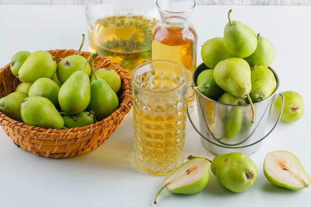 Pears in basket and bucket with drink high angle view on a white table