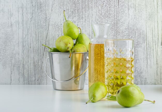 Pears with drink in a mini bucket on white and grungy wall, side view.