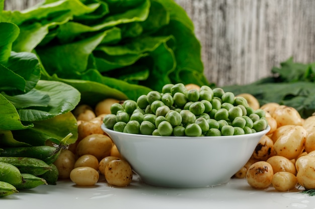 Peas with green pods, spinach, sorrel, lettuce in a bowl on white and grungy wall, side view.