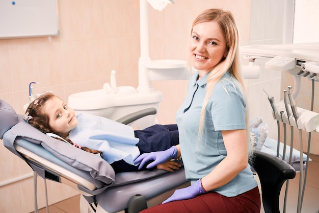 Free photo pediatric dentist sitting beside adorable little girl in dental office