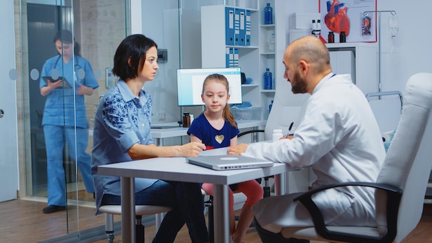 Pediatrician writing prescription for kid after examination. Healthcare practitioner, physician, specialist in medicine providing health care services consultation diagnostic treatment in hospital.