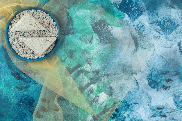 Free photo peeled sunflower seeds and sliced halva on the wooden plate on tulle , on the blue table.