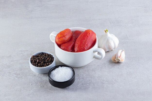 Peeled tomatoes with fresh garlics and spices placed on stone table. 