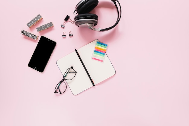 Pen on blank diary; eyeglasses; and stationery with mobile phone on pink background