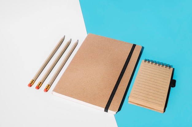 Free photo pencil; closed notebook and spiral notepad on white and blue backdrop