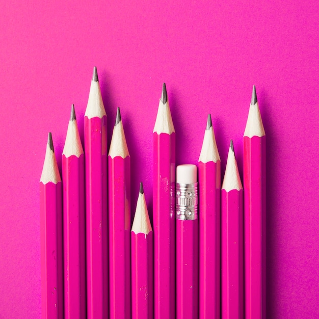 Pencil with eraser standing out from other sharp pencils on pink backdrop