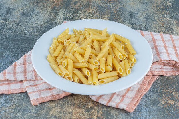 Penne pasta on the plate, on the towel , on the marble background.