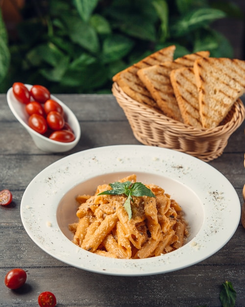 Free photo penne pasta in tomato sauce served with toast bread.