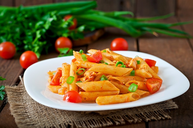 Penne pasta in tomato sauce with chicken and tomatoes  on a wooden table