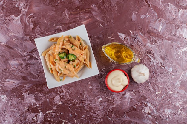 Free photo penne pasta with mayonnaise and fresh garlic on a light table.