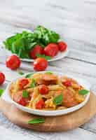 Free photo penne pasta with tomato sauce with sausage, tomatoes, green basil decorated in a frying pan on a wooden table