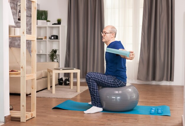 Pensioner doing sport with resistance band sitting on swiss ball