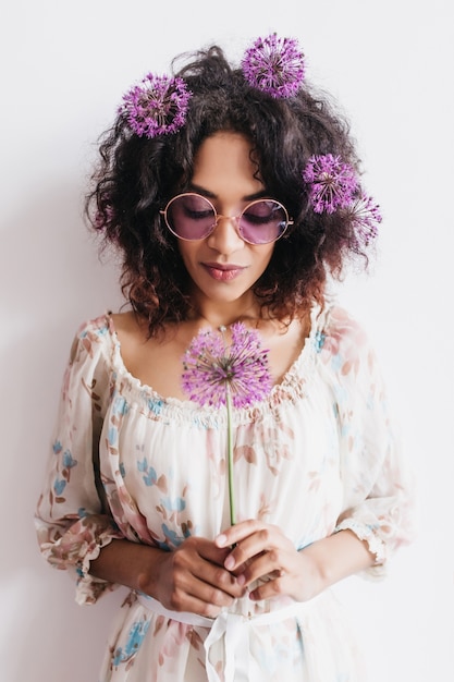 Free photo pensive african young woman posing with purple flower. relaxed black girl in glasses with allium.