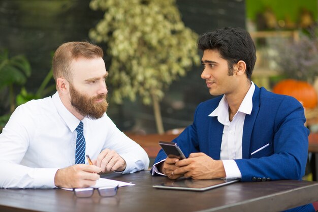 Pensive bearded man talking to business partner in modern cafe