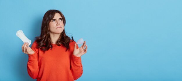 Pensive beautiful female wearing casual orange sweater looking away with thoughtful facial expression