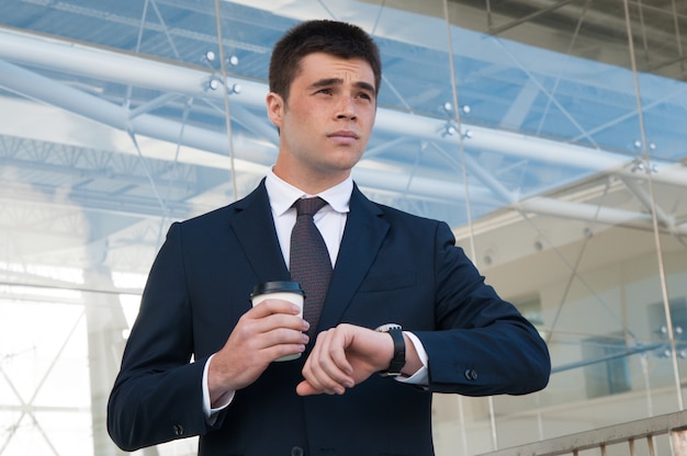 Pensive business man checking time on watch outdoors