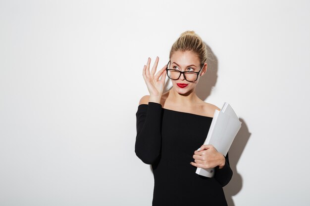 Pensive business woman in dress and eyeglasses holding documents