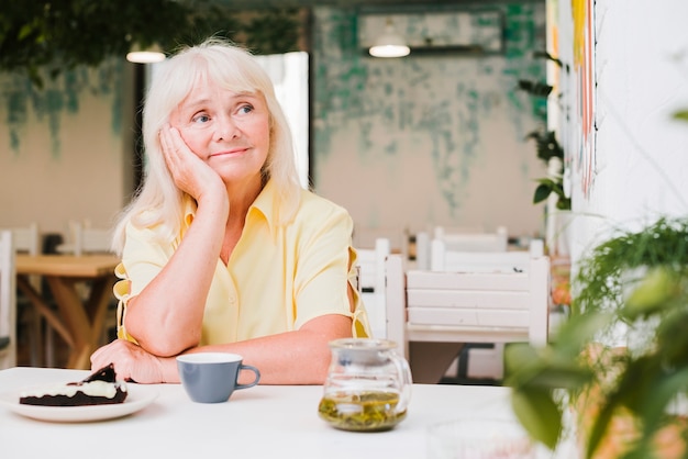 Pensive elderly woman sitting at table in cafe