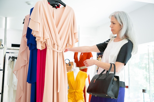 Free Photo pensive fashion store customer choosing clothes and browsing dresses on rack. medium shot, side view. fashion store or retail concept