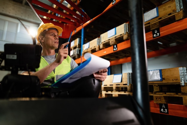 Pensive forklift operator examining stock of packages on shelves in a warehouse