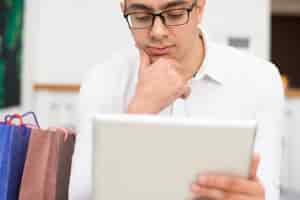 Free photo pensive man shopping and browsing on tablet computer