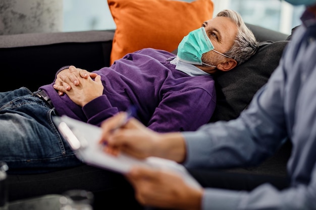 Free Photo pensive man wearing protective face mask while having counseling with his psychiatrist