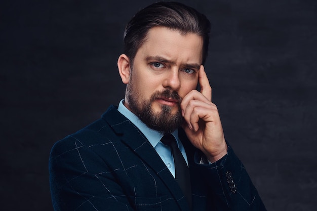 Free photo pensive middle-aged man with beard and hairstyle dressed in an elegant blue suit on a textured dark background in studio.