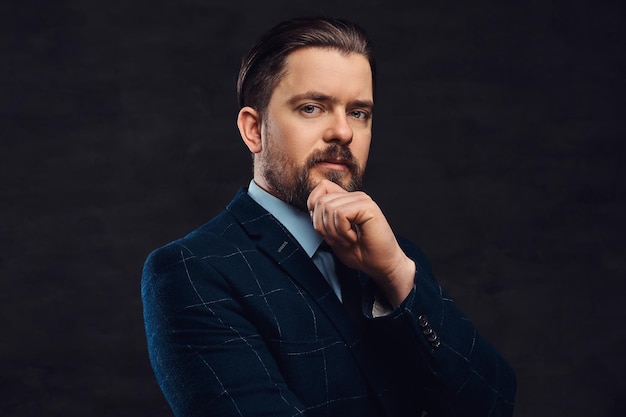 Free photo pensive middle-aged man with beard and hairstyle dressed in an elegant blue suit on a textured dark background in studio.