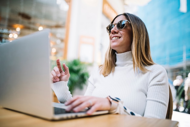 Pensive positive young woman using laptop at table in street cafe