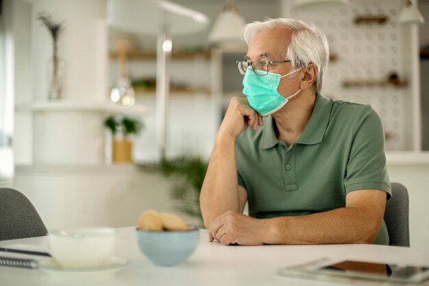 Pensive senior man with a face mask sitting at home and thinking of something