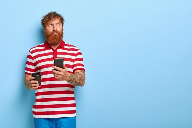 Free Photo pensive stylish ginger guy posing against the blue wall