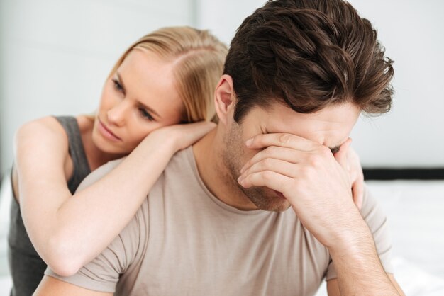 Pensive unhappy woman comfort her sad man while they sitting in bed